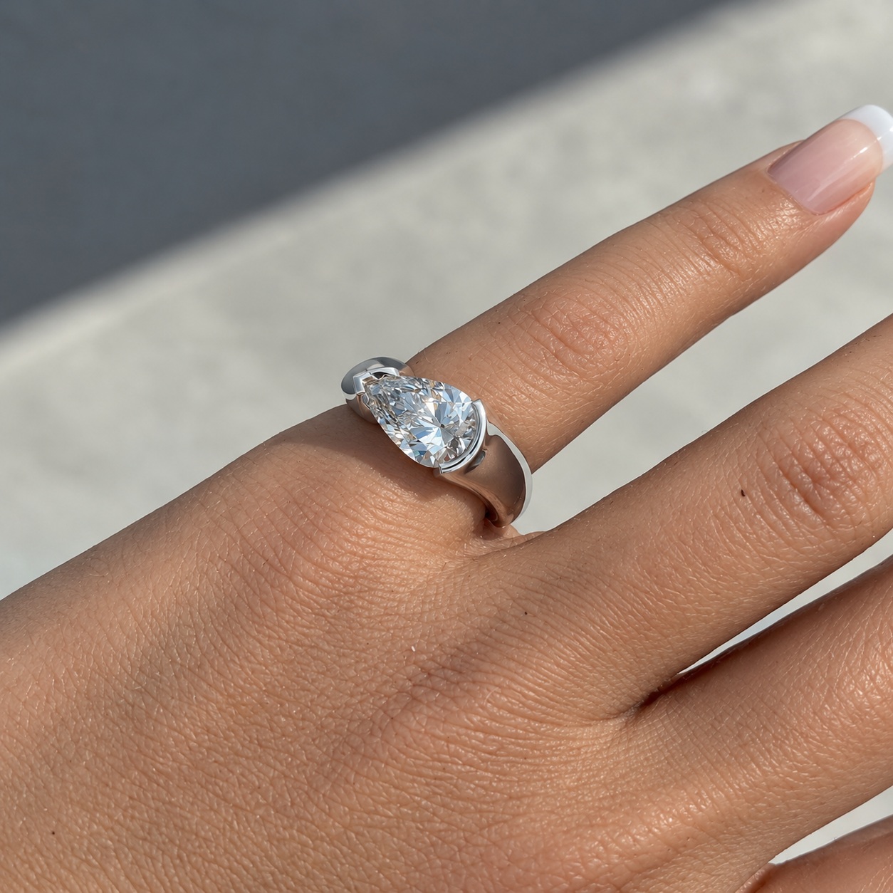 Close-up of a pear-cut diamond and the Poised Light tension band on a finger